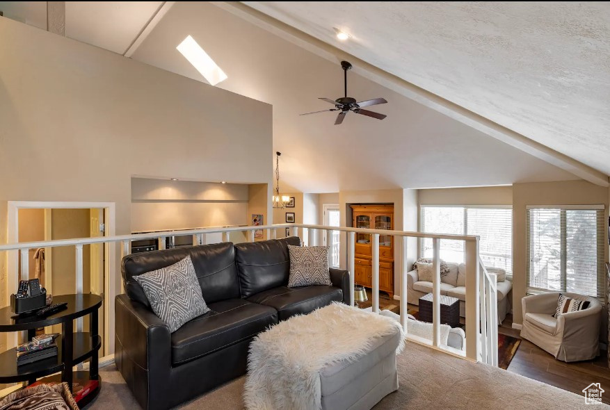 Living room with beam ceiling, high vaulted ceiling, dark hardwood / wood-style floors, a skylight, and ceiling fan with notable chandelier