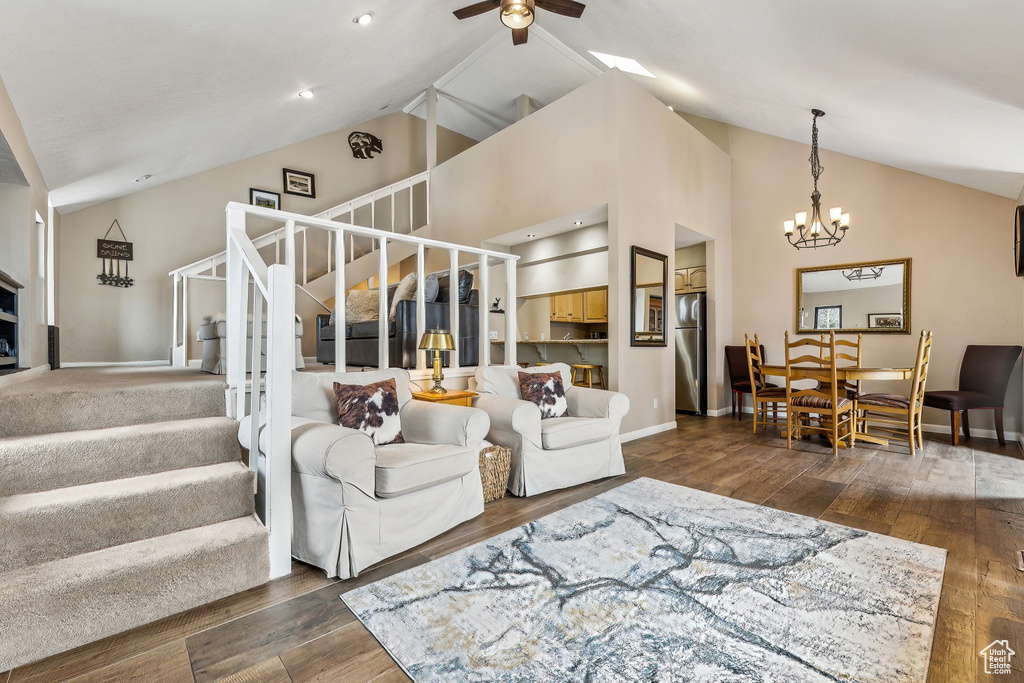 Living room featuring stairway, baseboards, high vaulted ceiling, hardwood / wood-style flooring, and ceiling fan with notable chandelier