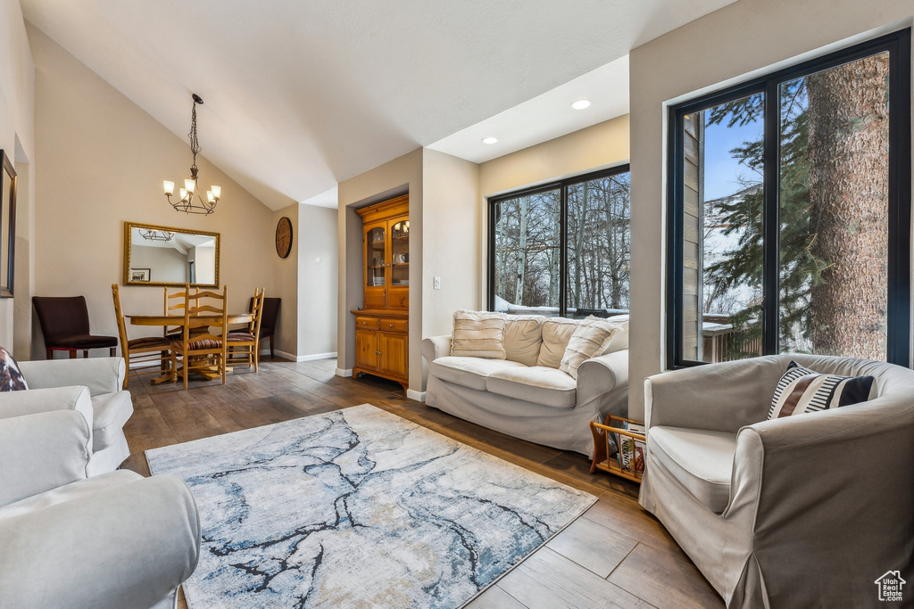 Living room with lofted ceiling, wood finished floors, recessed lighting, an inviting chandelier, and baseboards