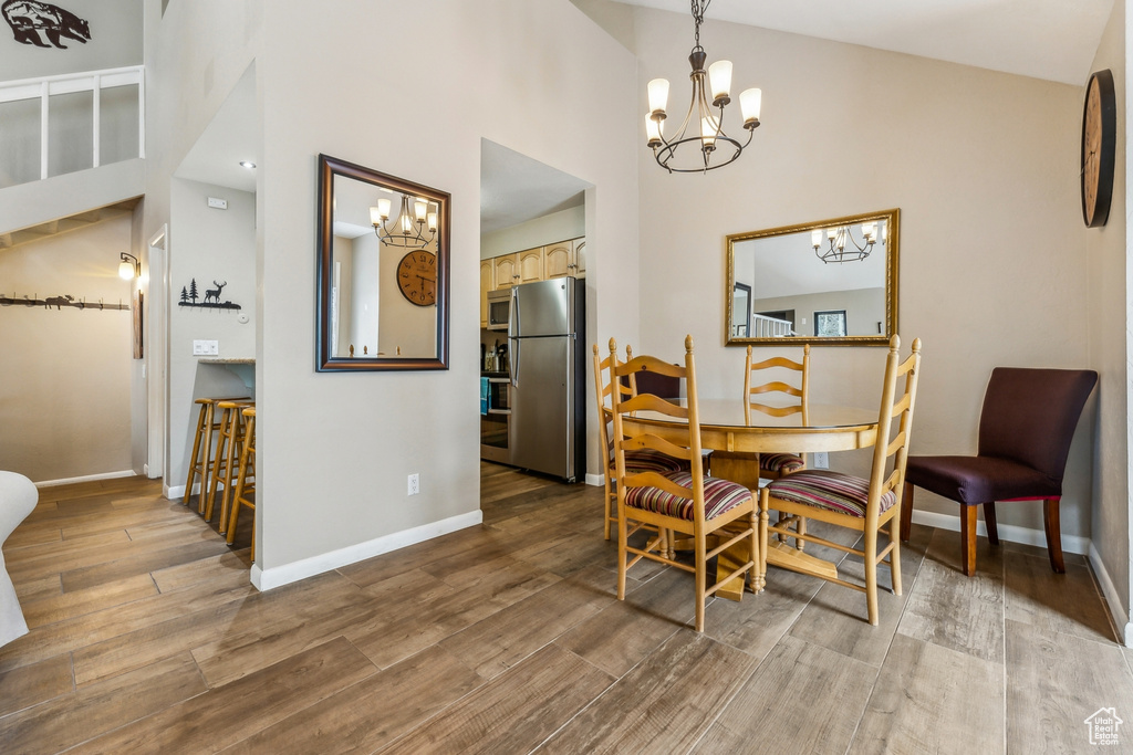 Dining space with an inviting chandelier, wood finished floors, baseboards, and high vaulted ceiling