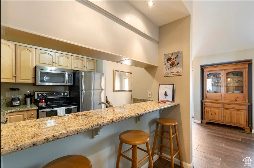 Kitchen with a breakfast bar area, stainless steel appliances, sink, light stone counters, and dark hardwood / wood-style flooring