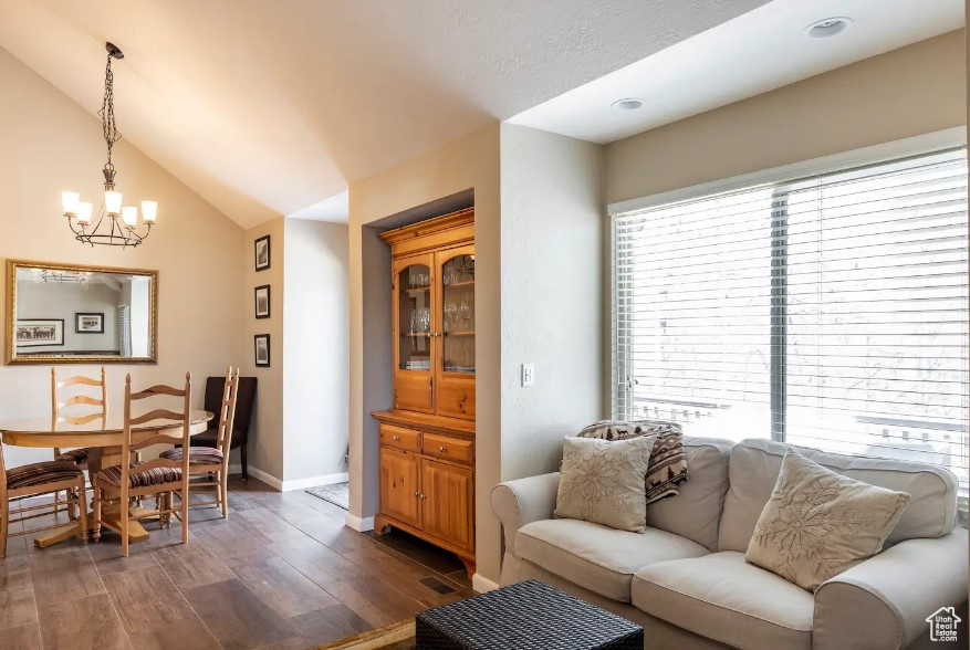 Living room featuring a notable chandelier, dark wood-type flooring, and vaulted ceiling