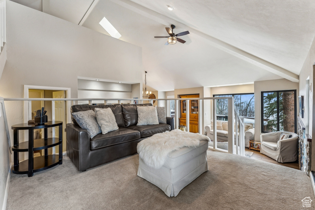 Carpeted living area with beam ceiling, a skylight, ceiling fan with notable chandelier, and high vaulted ceiling