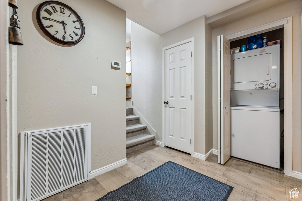 Interior space featuring light wood-type flooring, visible vents, stacked washer and clothes dryer, baseboards, and laundry area