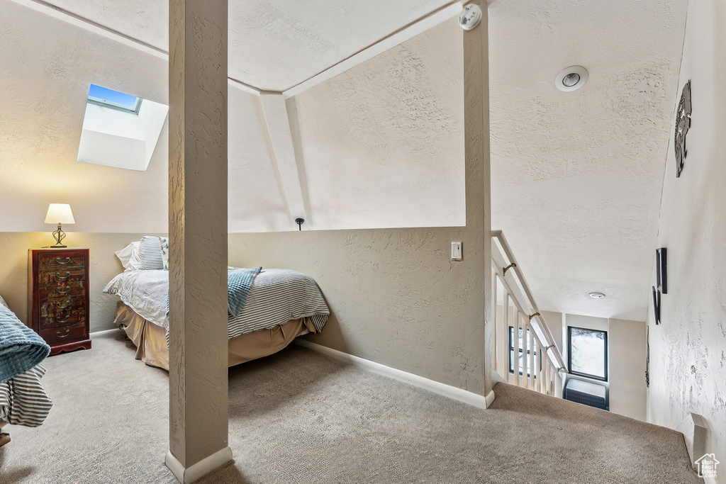 Carpeted bedroom featuring a textured ceiling, a skylight, baseboards, and a textured wall