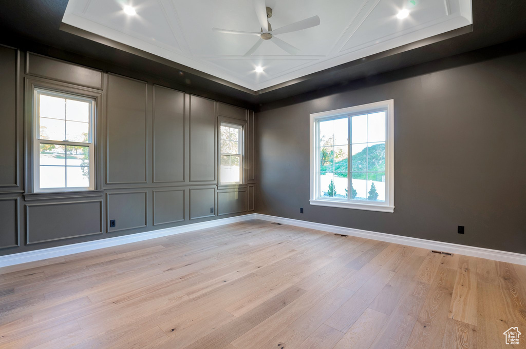 Empty room with light hardwood / wood-style flooring, a tray ceiling, and ceiling fan