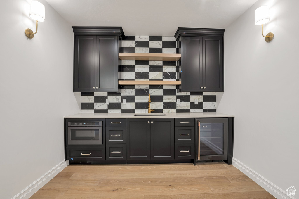 Kitchen featuring wine cooler, backsplash, stainless steel oven, and light wood-type flooring