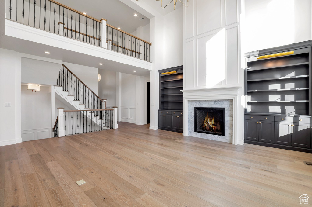 Unfurnished living room featuring built in features, light hardwood / wood-style flooring, and a towering ceiling