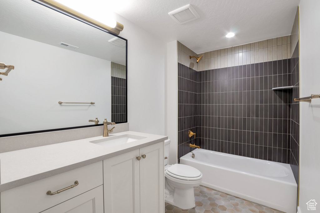 Full bathroom featuring vanity, tiled shower / bath combo, toilet, and tile patterned flooring