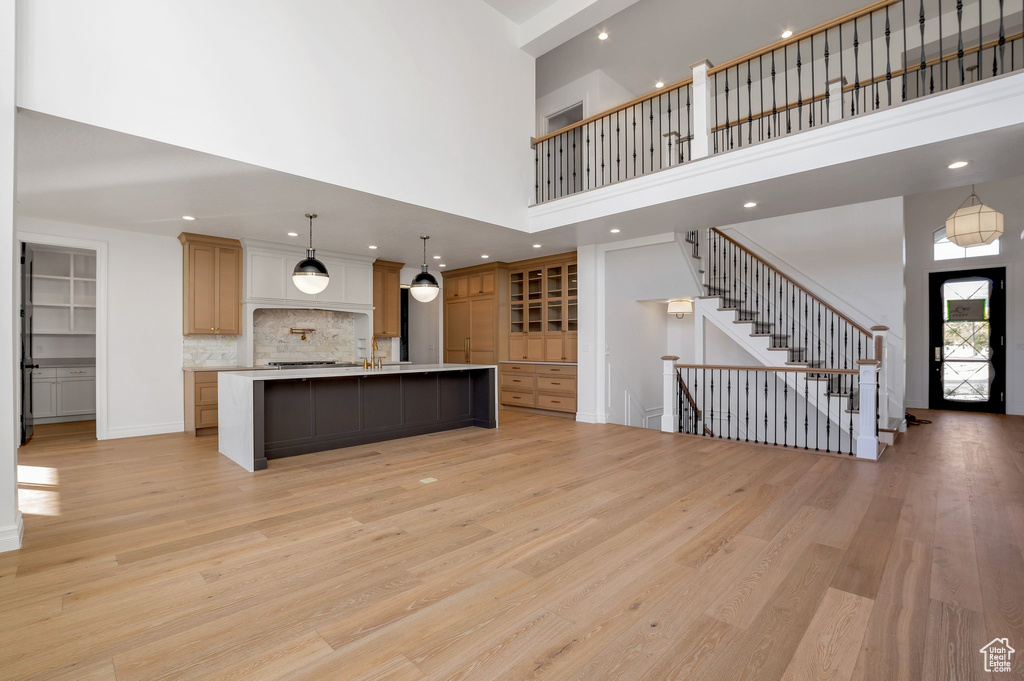 Kitchen featuring a large island with sink, a high ceiling, light hardwood / wood-style flooring, and hanging light fixtures