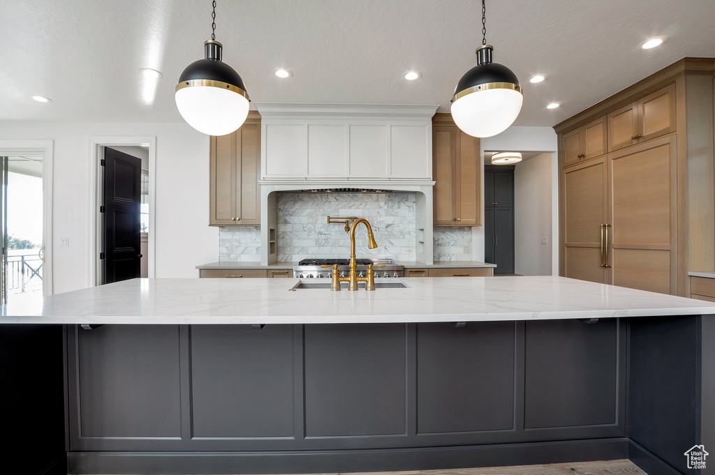 Kitchen with a large island, light stone counters, and decorative light fixtures