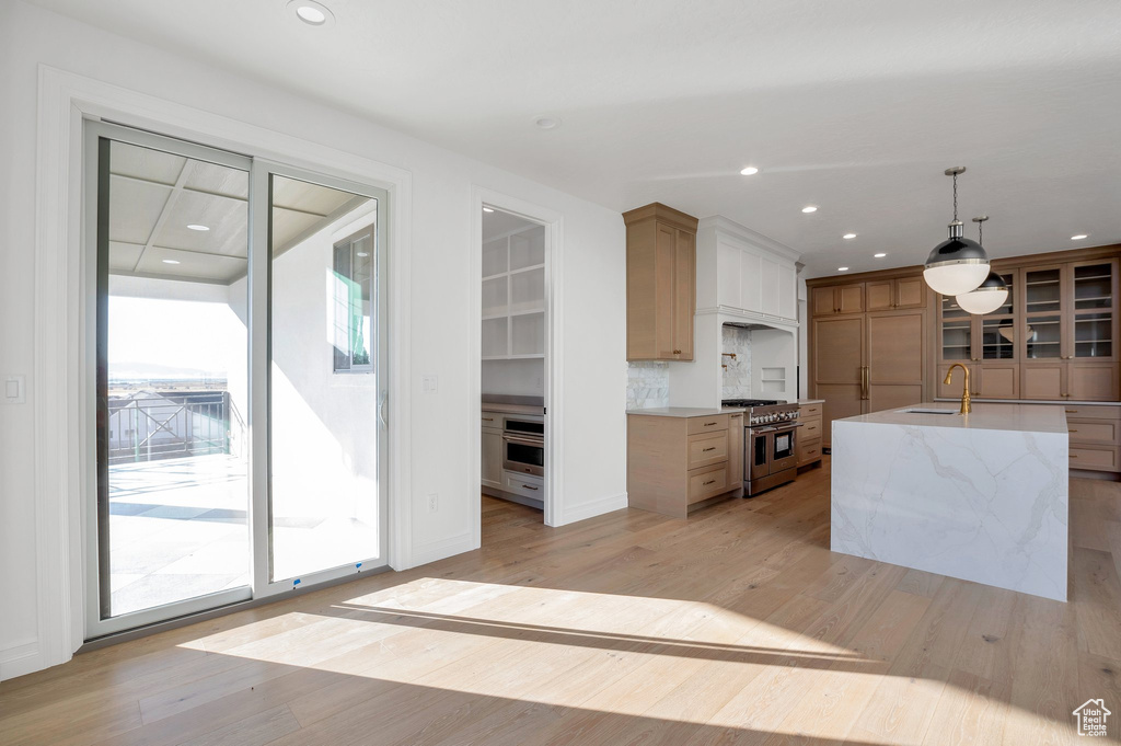 Kitchen with a center island with sink, appliances with stainless steel finishes, pendant lighting, light hardwood / wood-style floors, and sink