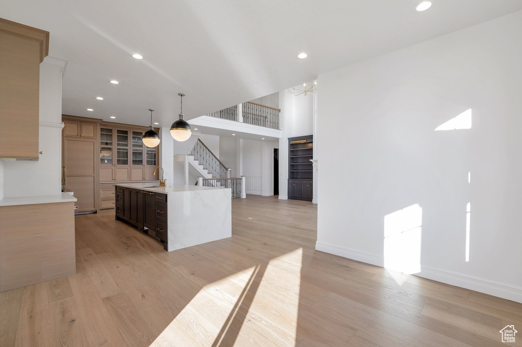 Kitchen featuring dark brown cabinets, a center island with sink, light wood-type flooring, decorative light fixtures, and sink