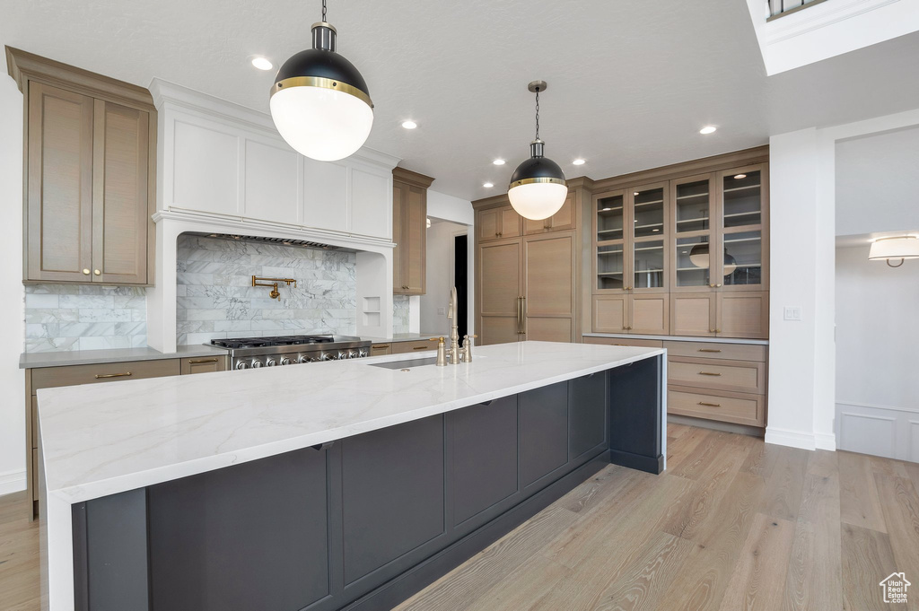 Kitchen with decorative backsplash, hanging light fixtures, sink, light stone countertops, and light hardwood / wood-style floors