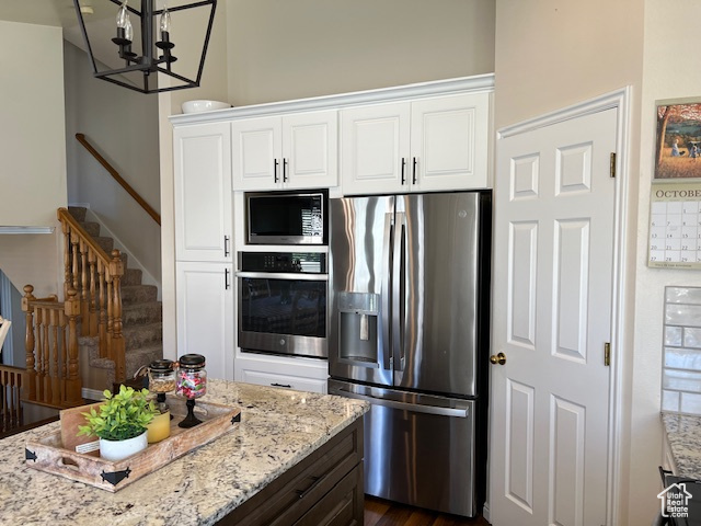 Kitchen featuring dark hardwood / wood-style floors, white cabinets, an inviting chandelier, appliances with stainless steel finishes, and light stone counters