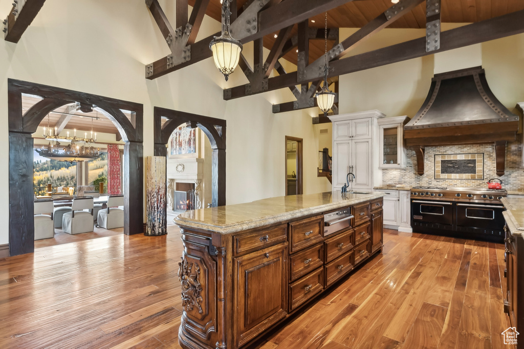 Kitchen featuring light hardwood / wood-style flooring, white cabinetry, high vaulted ceiling, and a center island with sink