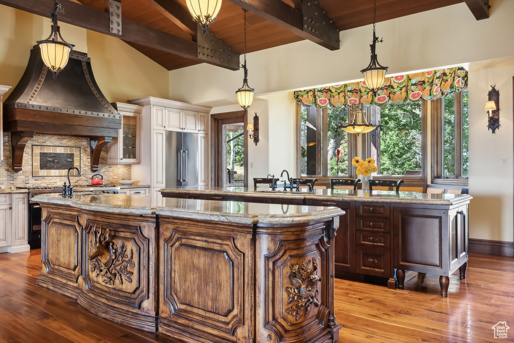 Kitchen with high end fridge, pendant lighting, a center island with sink, and hardwood / wood-style floors