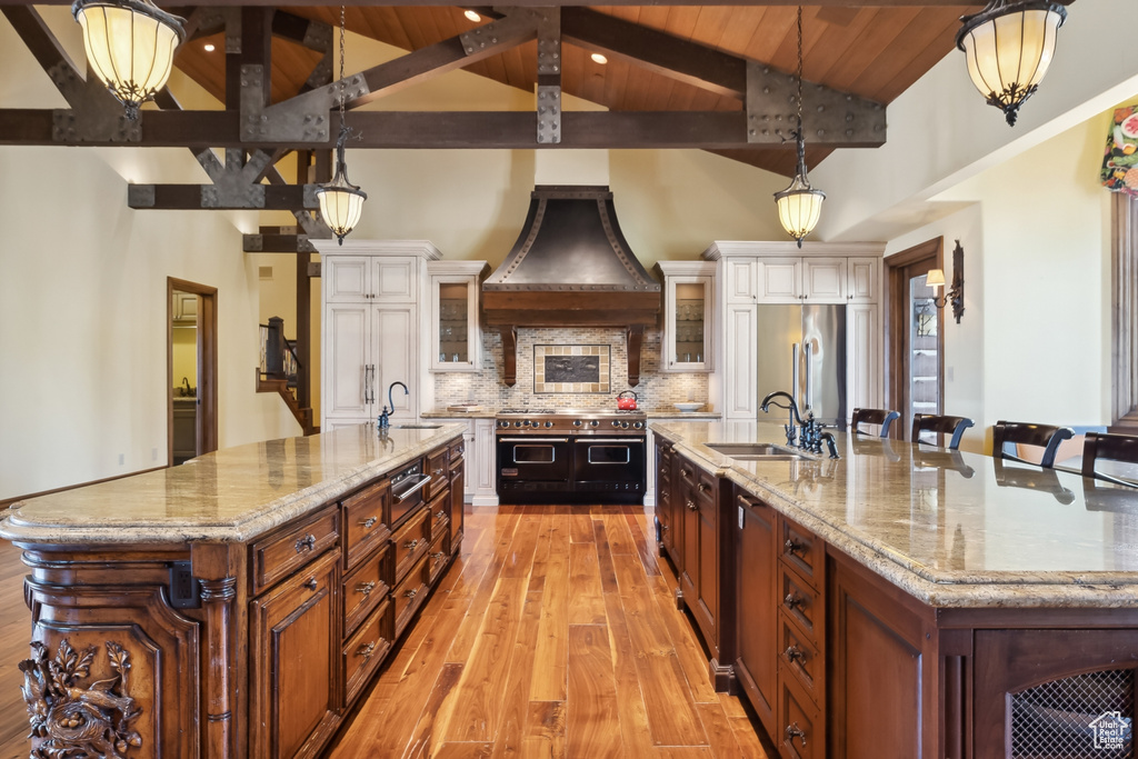 Kitchen featuring a large island with sink, sink, light hardwood / wood-style floors, stainless steel appliances, and decorative light fixtures