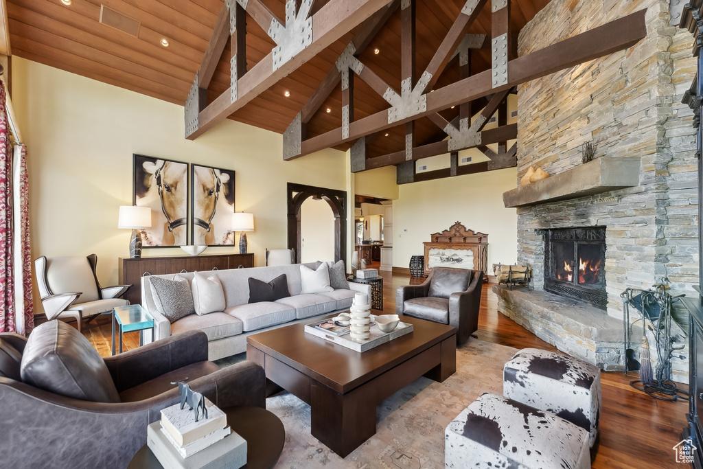 Living room featuring wood ceiling, beam ceiling, high vaulted ceiling, wood-type flooring, and a stone fireplace