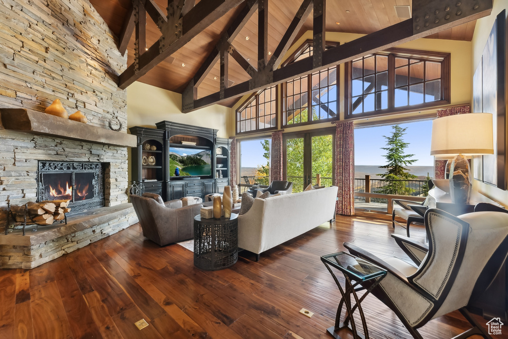 Living room with a stone fireplace, beam ceiling, high vaulted ceiling, and wood-type flooring