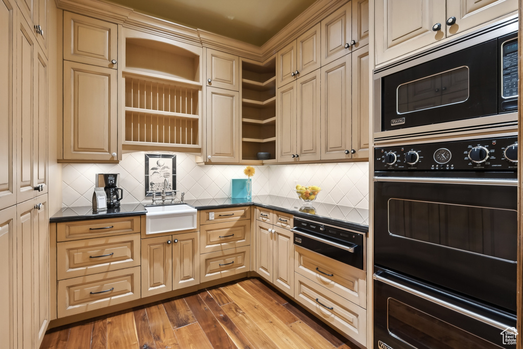 Kitchen with decorative backsplash, stainless steel microwave, hardwood / wood-style flooring, sink, and black double oven