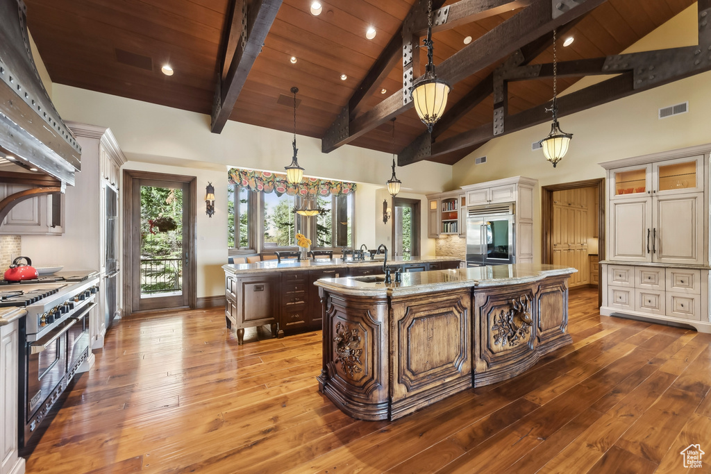 Kitchen featuring a center island with sink, high end appliances, hardwood / wood-style floors, light stone countertops, and high vaulted ceiling