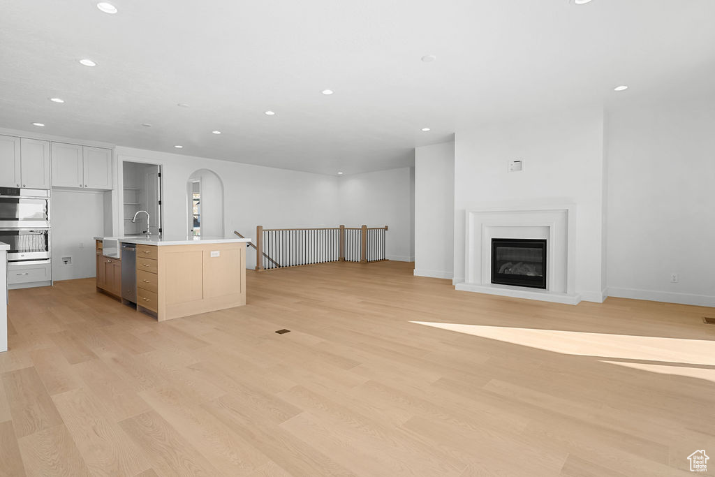 Kitchen with white cabinets, a center island with sink, appliances with stainless steel finishes, light hardwood / wood-style floors, and sink