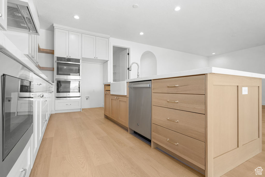 Kitchen featuring ventilation hood, white cabinetry, light hardwood / wood-style flooring, and stainless steel appliances