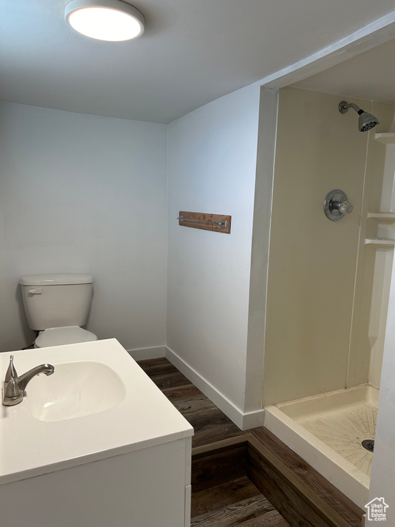 Bathroom with toilet, vanity, wood-type flooring, and a shower