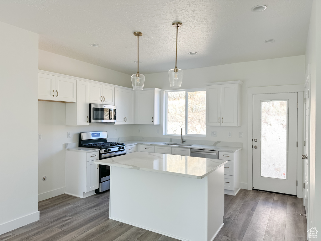 Kitchen featuring appliances with stainless steel finishes, a kitchen island, pendant lighting, white cabinets, and light hardwood / wood-style flooring