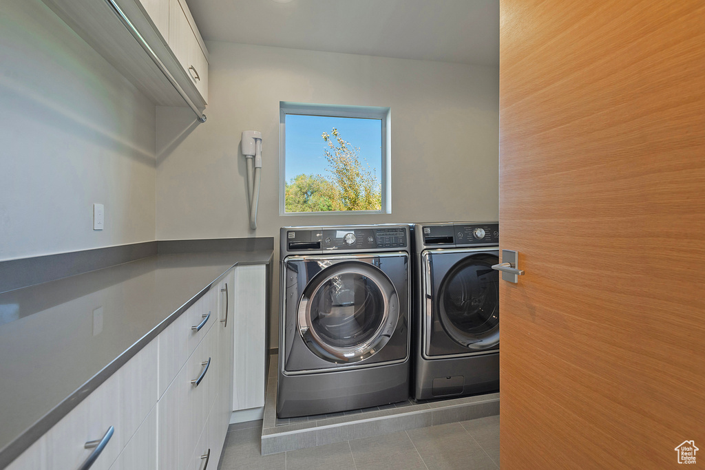 Laundry room with washing machine and clothes dryer, light tile patterned floors, and cabinets