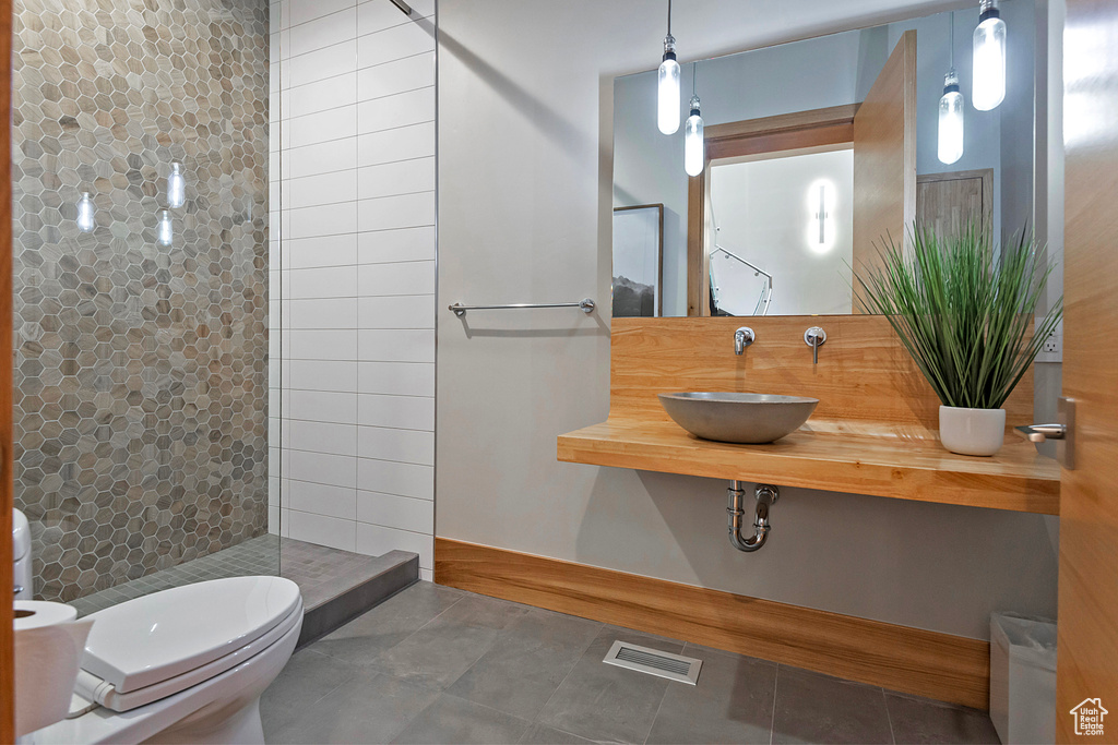 Bathroom with tiled shower, sink, toilet, and tile patterned floors