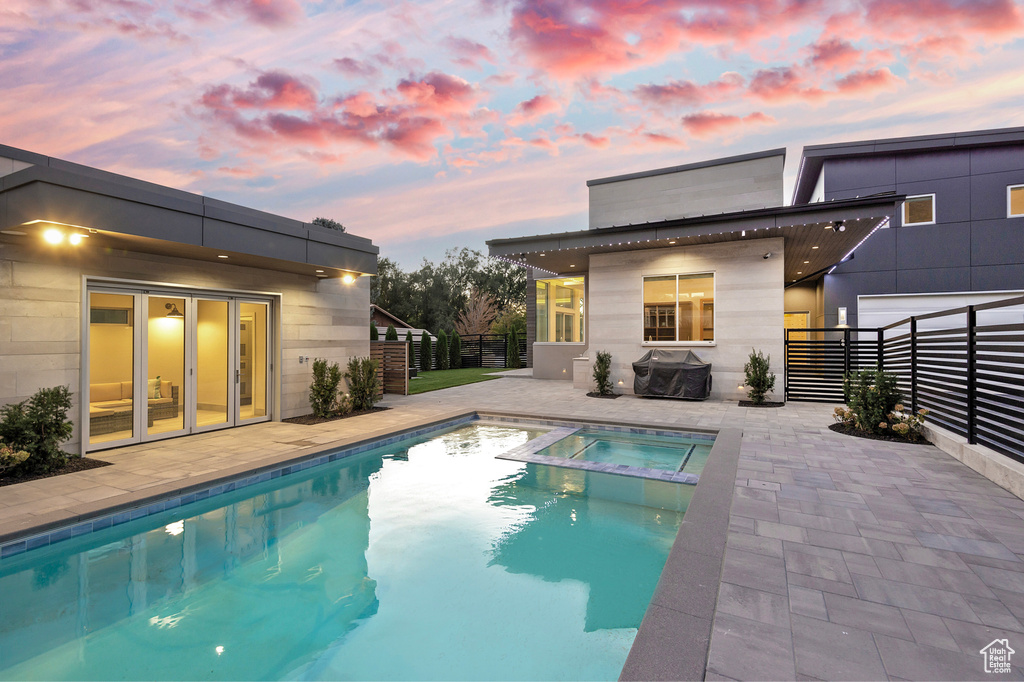 Pool at dusk with an in ground hot tub, a patio area, and area for grilling