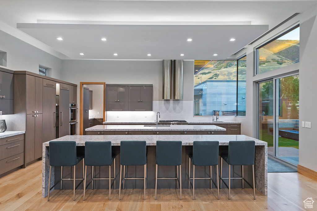 Kitchen with a large island with sink, a kitchen breakfast bar, light stone counters, and light hardwood / wood-style floors