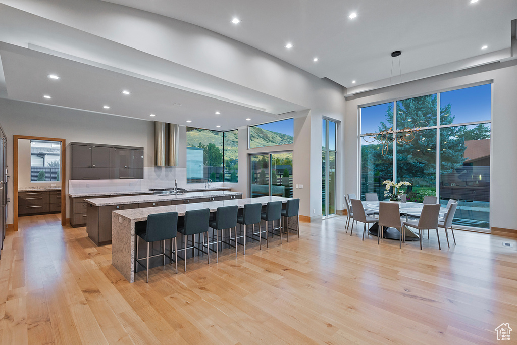 Kitchen with hanging light fixtures, light stone counters, a kitchen breakfast bar, light wood-type flooring, and sink