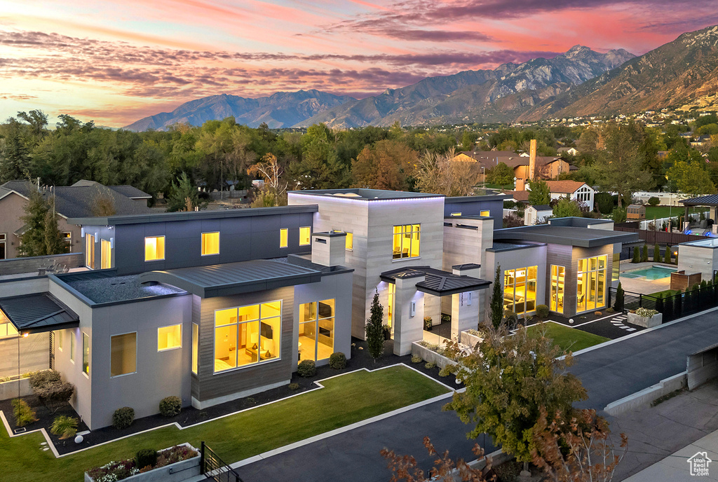 Back house at dusk featuring a mountain view and a lawn