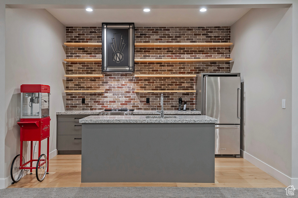 Bar with high end refrigerator, gray cabinetry, brick wall, sink, and light wood-type flooring