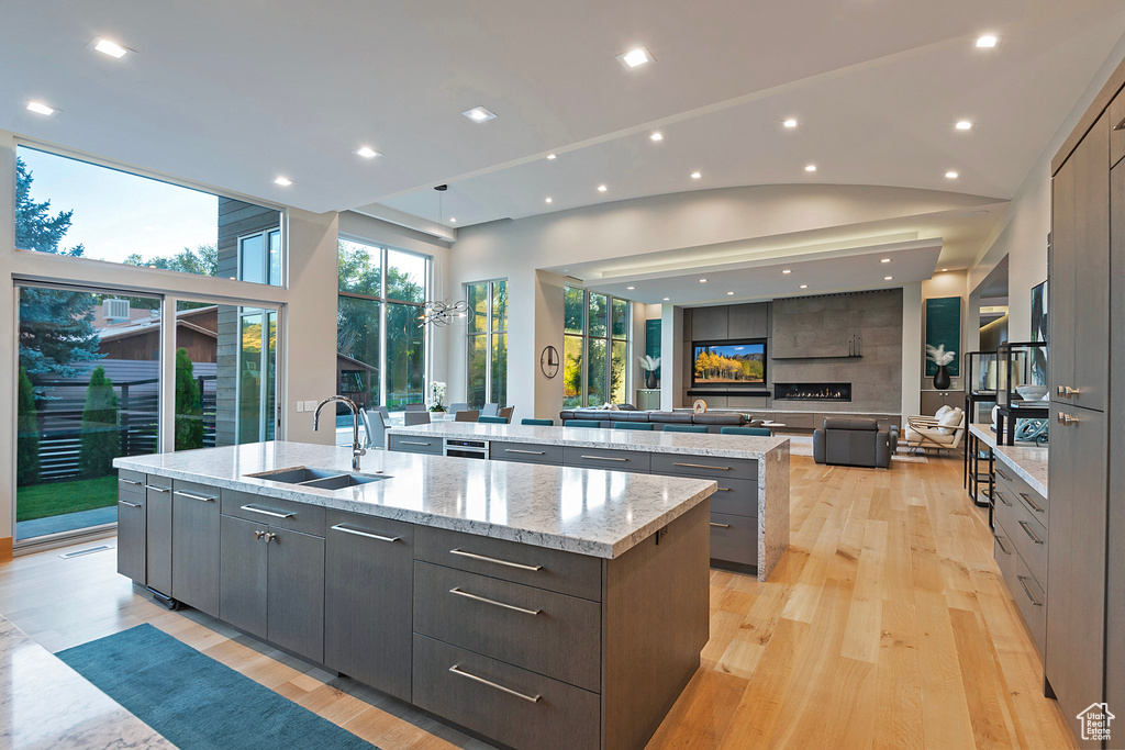 Kitchen with light hardwood / wood-style floors, a large island, sink, light stone countertops, and high vaulted ceiling