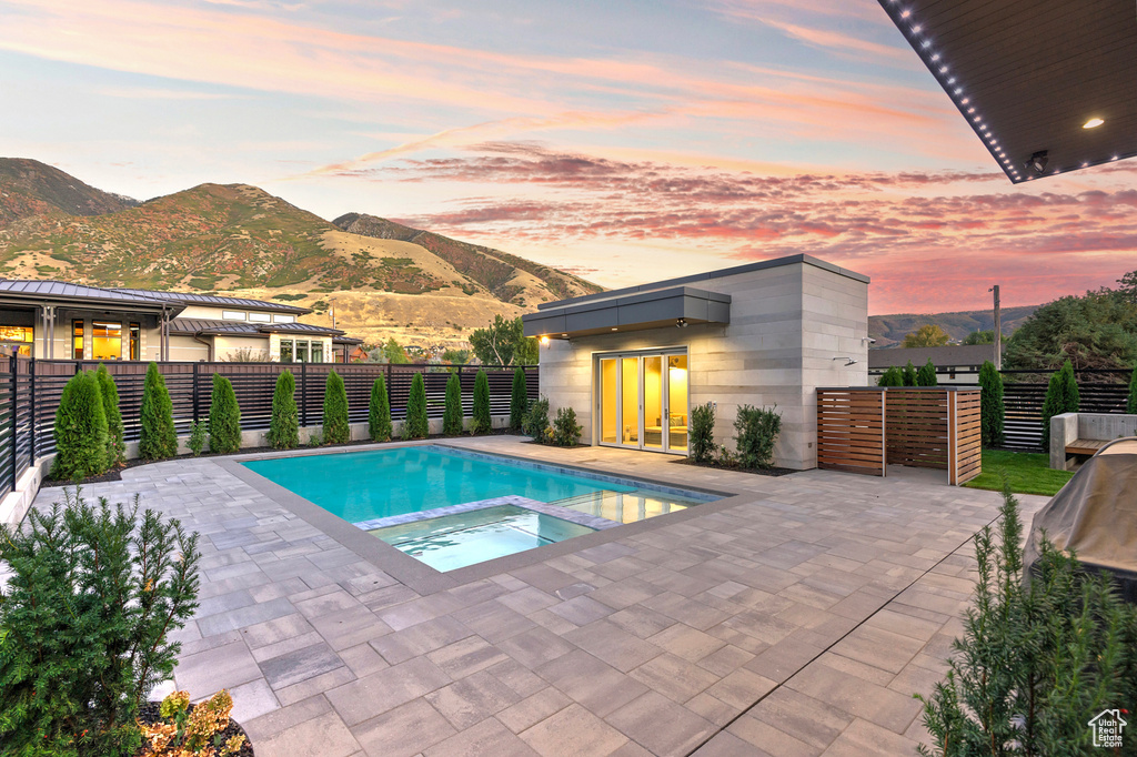 Pool at dusk featuring a patio area, a mountain view, and an in ground hot tub