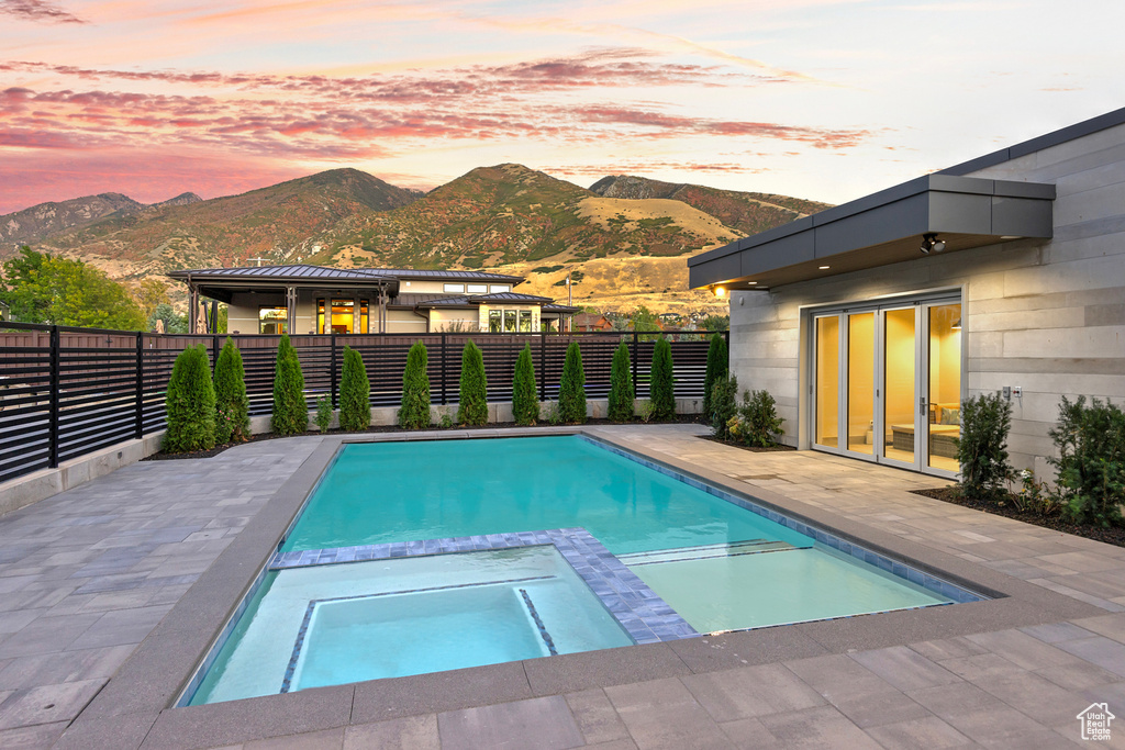 Pool at dusk featuring an in ground hot tub, a mountain view, and a patio