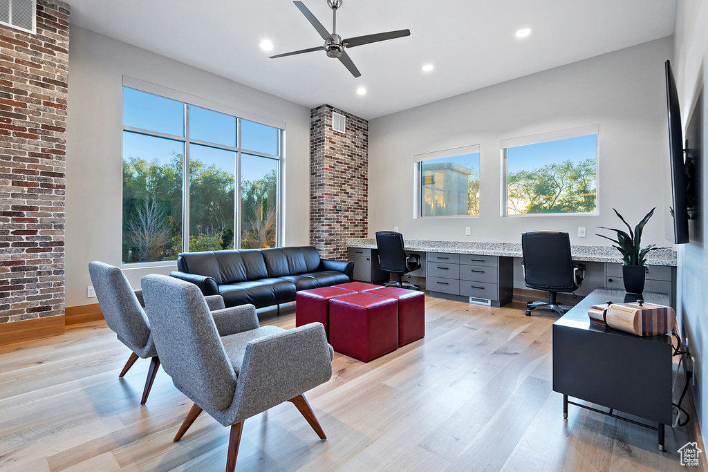 Living room featuring built in desk, light hardwood / wood-style floors, brick wall, and ceiling fan