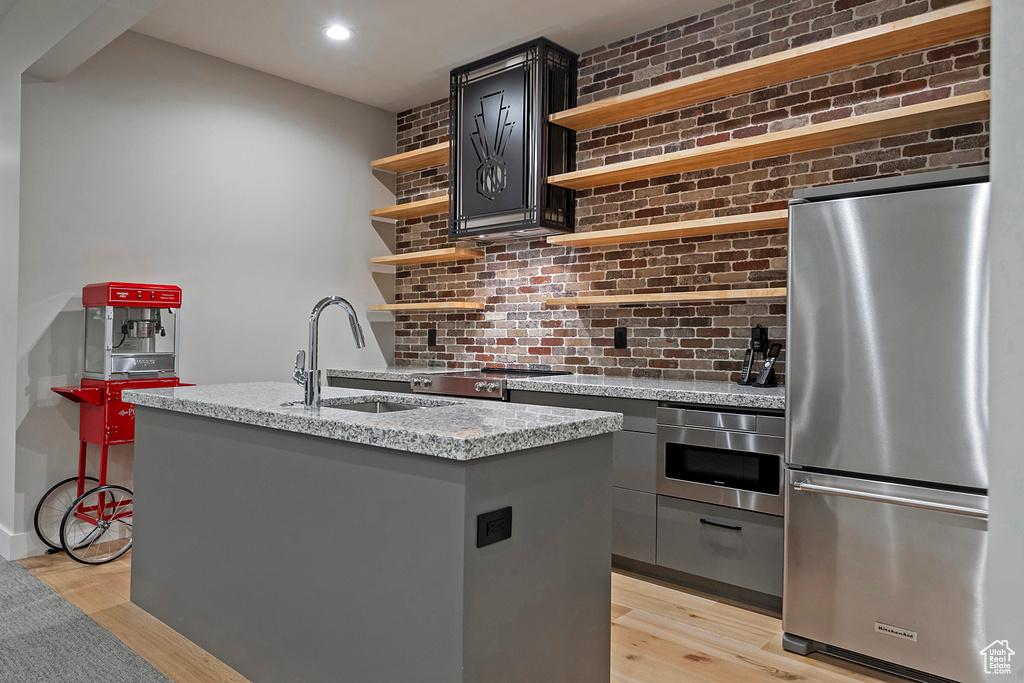 Kitchen featuring sink, stainless steel appliances, light stone counters, light hardwood / wood-style flooring, and a center island with sink