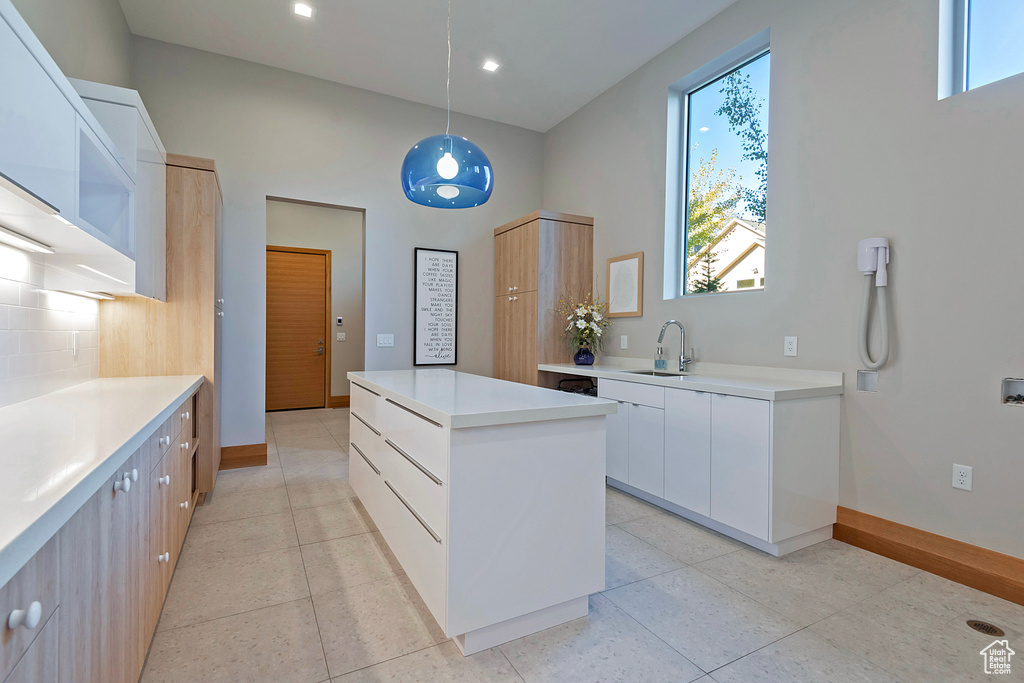 Kitchen with white cabinets, a kitchen island, backsplash, pendant lighting, and sink