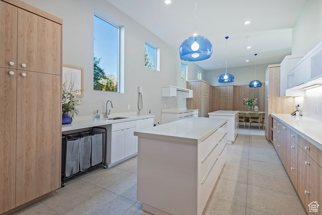 Kitchen featuring light brown cabinets, white cabinetry, sink, pendant lighting, and a center island