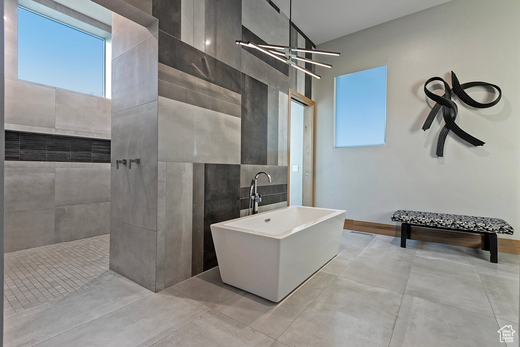 Bathroom with tile walls, tile patterned floors, shower with separate bathtub, and an inviting chandelier