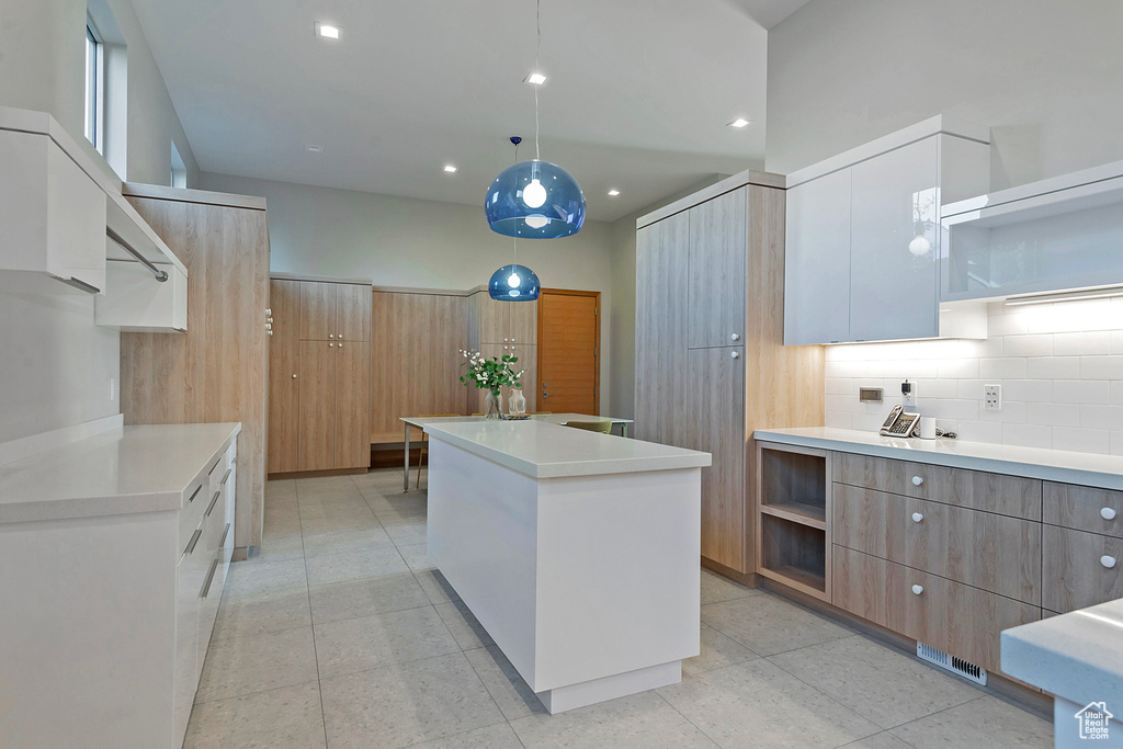 Kitchen with light tile patterned flooring, a kitchen island, pendant lighting, white cabinets, and decorative backsplash