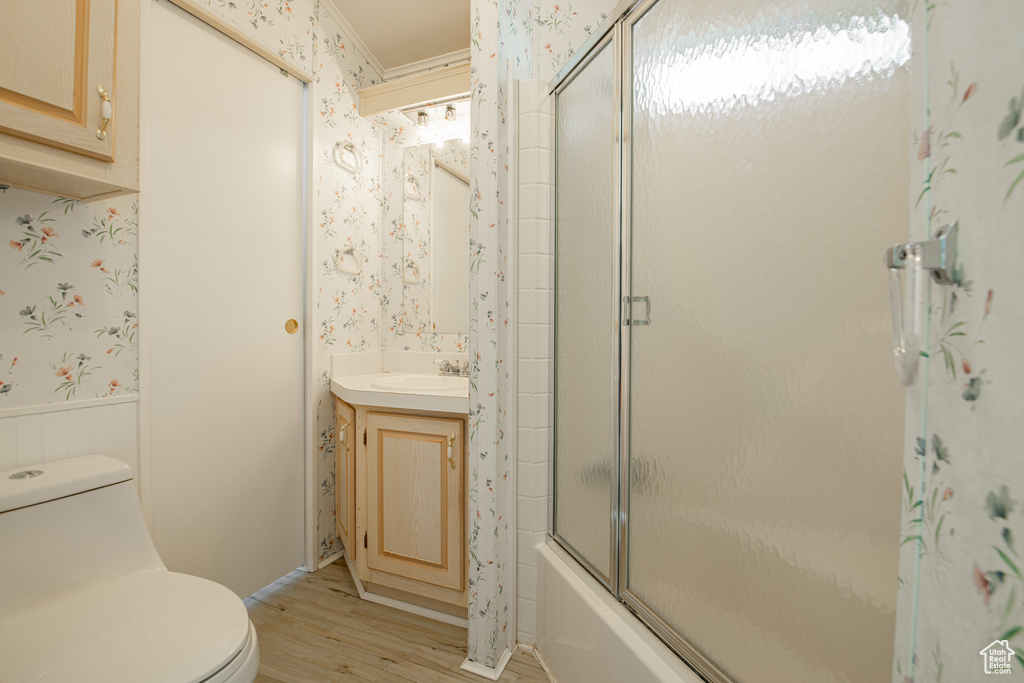 Full bathroom with vanity, toilet, hardwood / wood-style flooring, and bath / shower combo with glass door