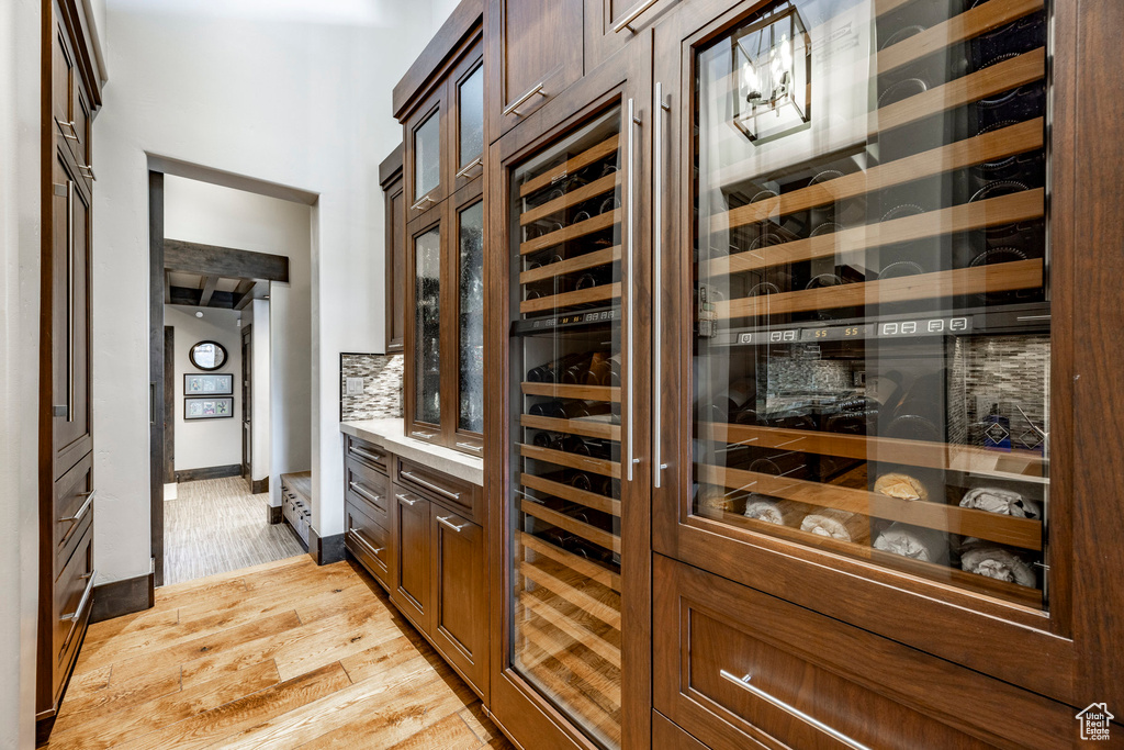 Wine cellar with light wood-style flooring, baseboards, and wine cooler