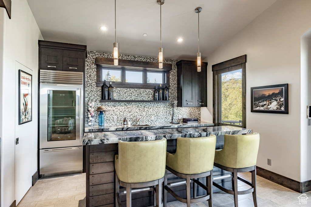 Kitchen with built in refrigerator, decorative backsplash, baseboards, recessed lighting, and a kitchen breakfast bar
