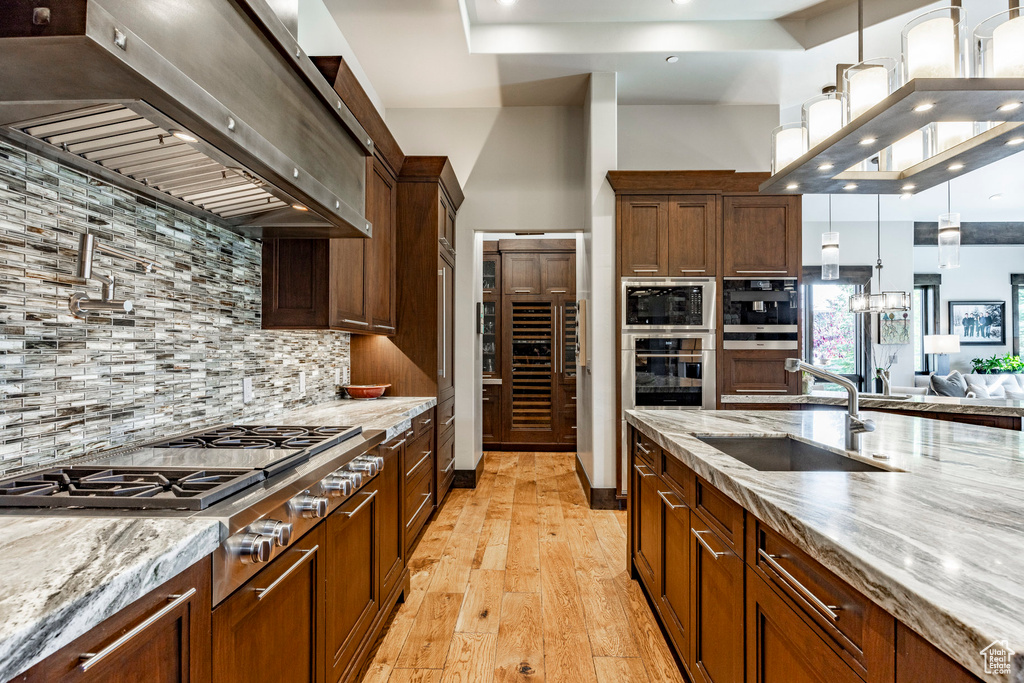 Kitchen with wall chimney exhaust hood, a sink, stainless steel appliances, backsplash, and light wood-style flooring